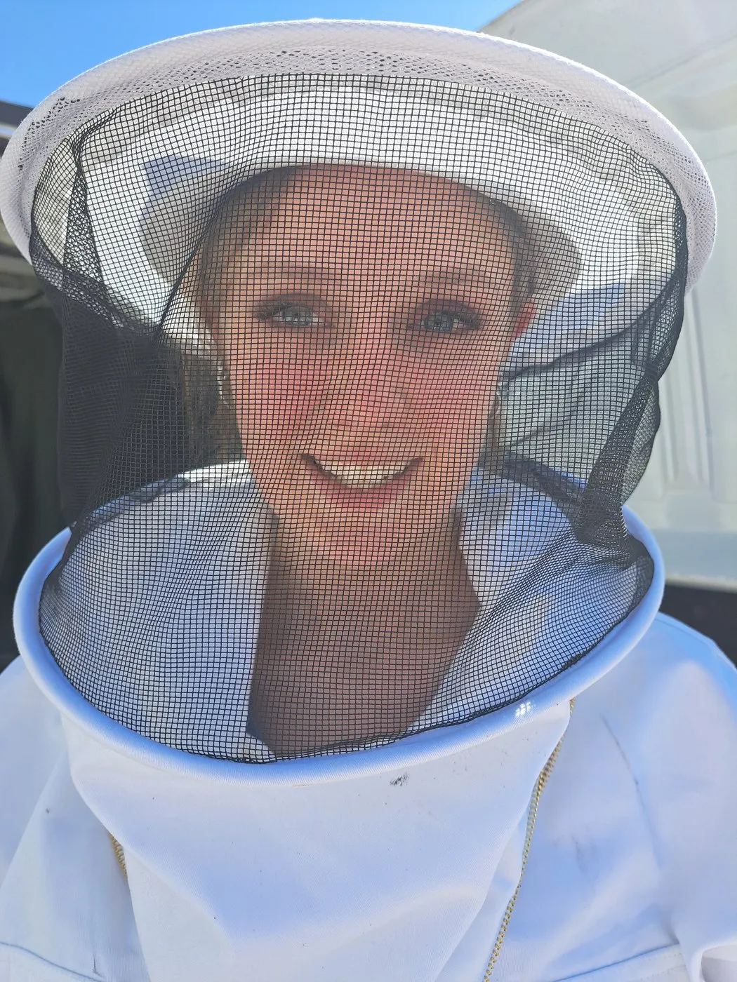 Little Bear smiling through a white bee veil after harvest work